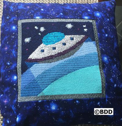 A pillow with an alien spaceship on it.