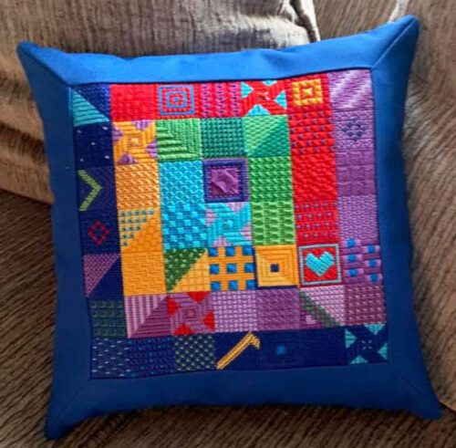 A blue pillow with colorful squares and crosses on it.