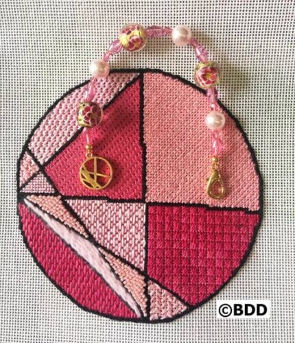 A pink cross stitch ornament with peace sign and pearls.