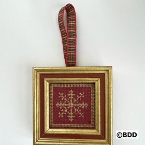 A red and gold framed ornament hanging on a wall.