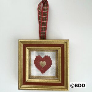 A cross stitch heart hanging in a gold frame.