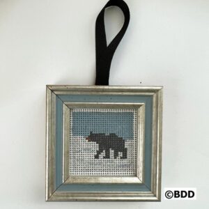 A bear cross stitch ornament hanging on a wall.