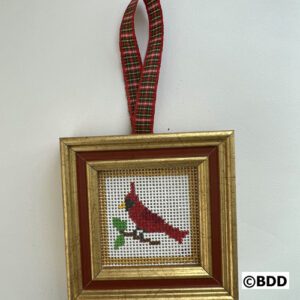 A framed needlepoint cardinal hanging on the wall.