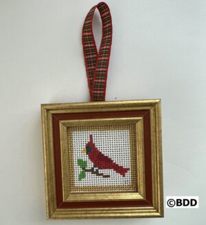 A framed needlepoint cardinal hanging on the wall.