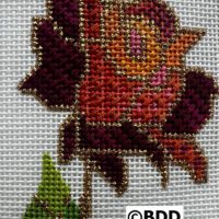 A cross stitch of a rose with leaves.