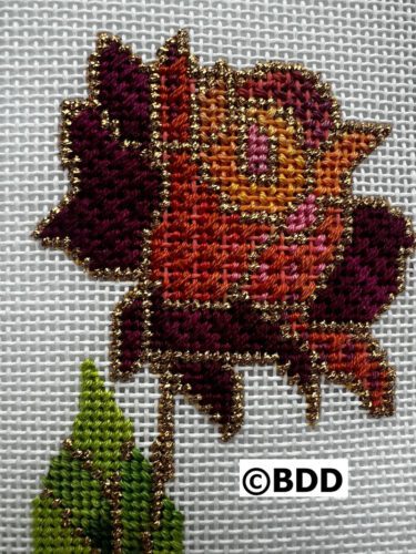 A cross stitch of a rose with leaves.